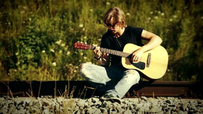 戴着墨镜的长发年轻人坐在铁路上弹吉他