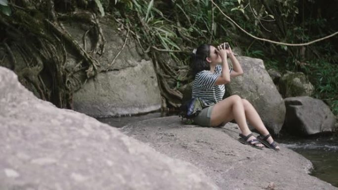 一个亚洲女孩拿着望远镜坐在一块石头上。
