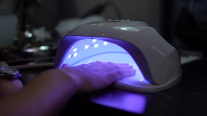 女人在指甲护理沙龙用紫外线灯用虫胶干燥指甲，特写