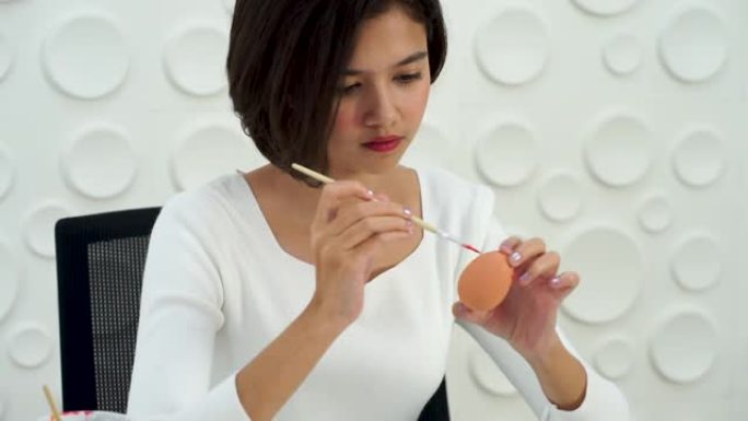 泰国亚裔女青年在屋内用彩笔画复活节彩蛋