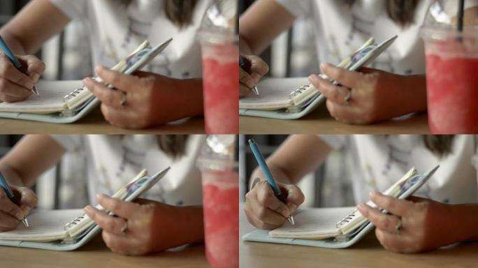 亚洲妇女坐着写日记，用一杯冰沙果汁激发饮料店的生活。