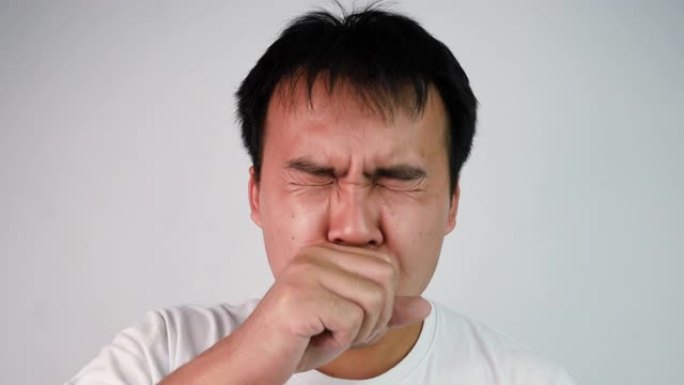 在灰色背景上，穿着白色t恤咳嗽和喉咙痛的亚洲病人的特写肖像。男性面对流感症状。