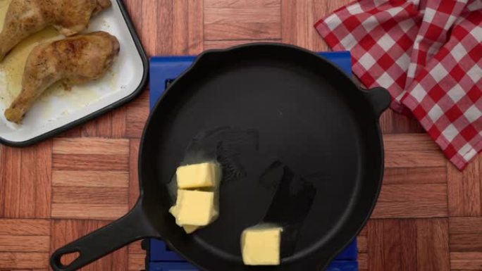 女厨师正在将黄油放在锅上，在煤气炉上近距离拍摄铁锅，大块黄油在烤架上融化。