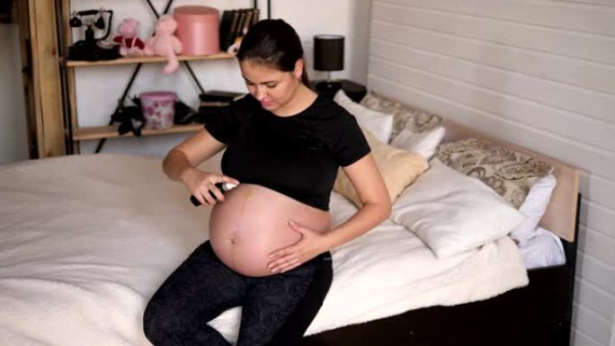 Pregnant woman is applying moisturizing body oil o