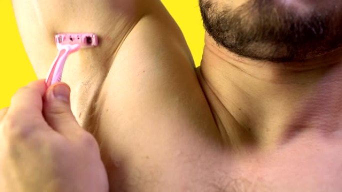 一个年轻人用粉红色的织布机剃毛腋窝。特写