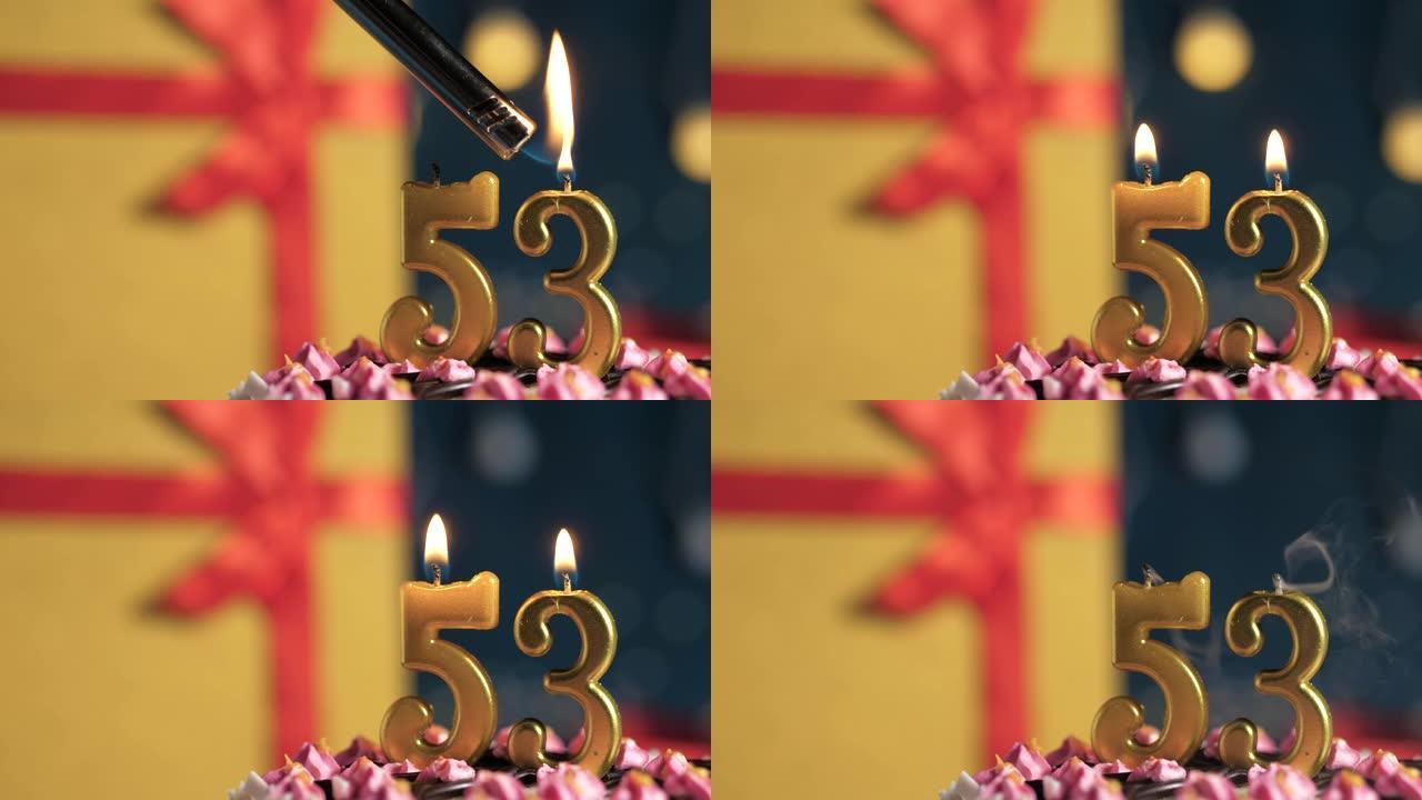 生日蛋糕编号53点灯燃烧的金色蜡烛，蓝色背景礼物黄色盒子用红丝带绑起来。特写和慢动作