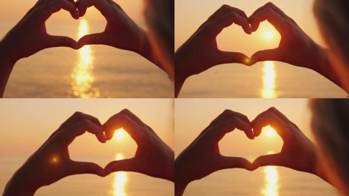 女性的手在海面上显示出心脏的形状，太阳升起的地方。美丽的浪漫场景