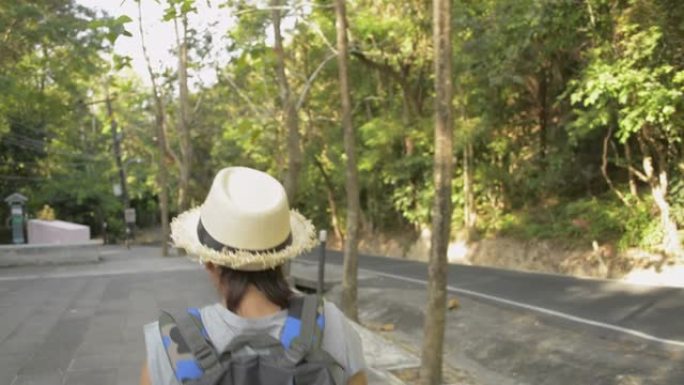 亚洲女性徒步旅行者背着背包穿过热带雨林的后视图。戴草帽的女人走在小路上。