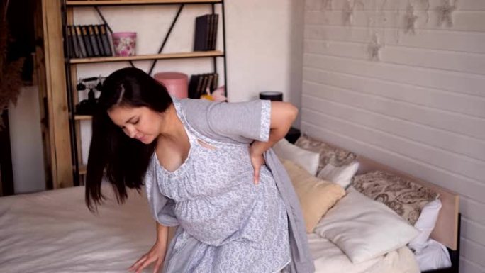 悲伤的孕妇在卧室里穿着睡衣肚子疼或背痛。