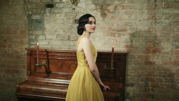 年轻女子手指波浪发型明亮的妆容站在钢琴蜡烛附近浪漫燃烧。黑发长复古金色晚装复古风格30年代连衣裙。背