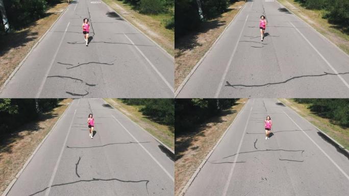 穿着粉色衬衫的漂亮苗条女孩正在练习跑步。戴着耳机的年轻黑发女人在炎热的夏日在公园锻炼