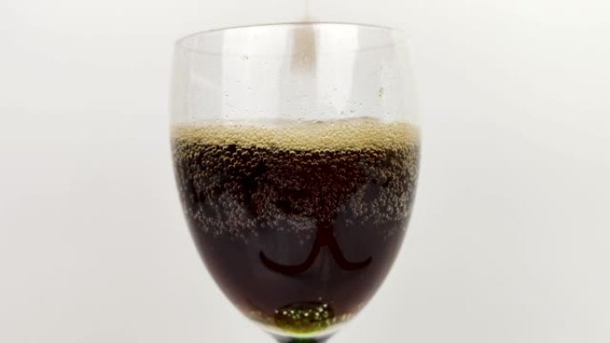 苏打水正在倒入玻璃杯中。微距视频，将深色饮料倒入透明杯子中。