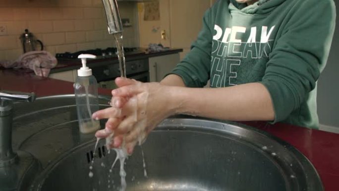 在新型冠状病毒肺炎危机期间，小孩用大量肥皂用厨房水槽洗手。