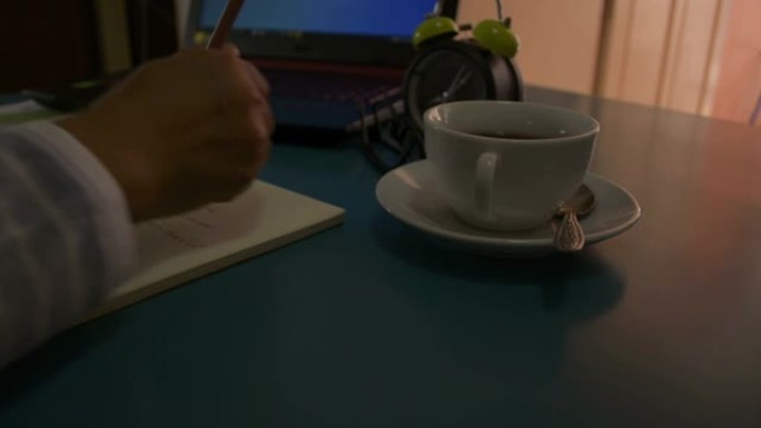 用笔记本电脑在桌子上工作的女商人。女人的手在记事本上写字，在家喝一杯咖啡。