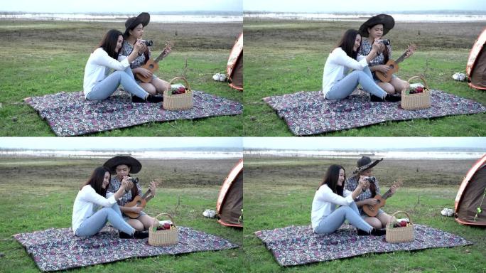 两个快乐的女孩在帐篷里玩尤克里里拍智能手机自拍自拍照片