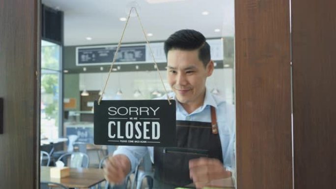 亚洲青少年企业家男子早上在他的咖啡馆里打开招牌。亚洲业主在场展示符号。商业、展览和表达的概念。