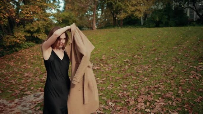 女人走过一个秋天的公园，很冷，穿着棕色外套保暖