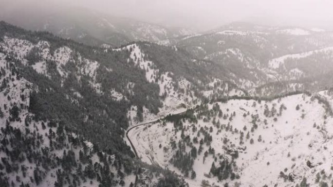 在暴风雪中飞过白雪覆盖的山上。科罗拉多州博尔德外的无人机鸟瞰图。洛矶山脉上方的森林，云层和树木的4k