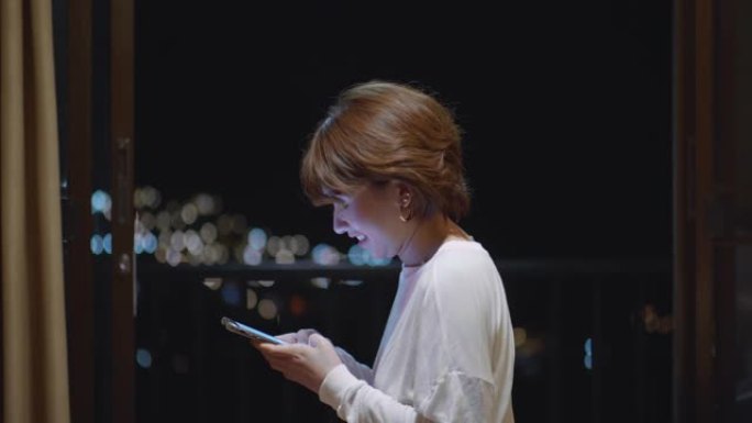 年轻的亚洲妇女坐在阳台上并在智能手机上工作