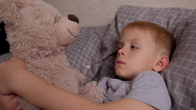 一个患水痘的小男孩和他最喜欢的泰迪熊躺在床上。