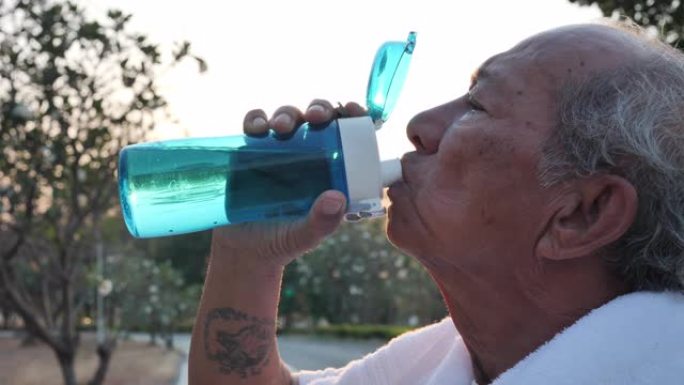 在晚上有阳光的公园运动后，关闭亚洲老年人喝水。健康生活方式和运动理念。慢动作