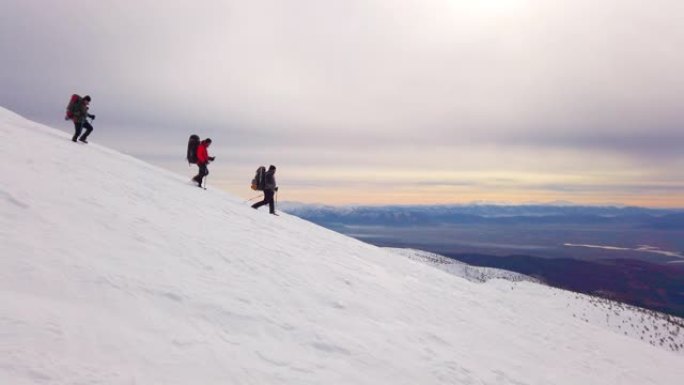 高山登山队在日出时行走在冬季高海拔山峰