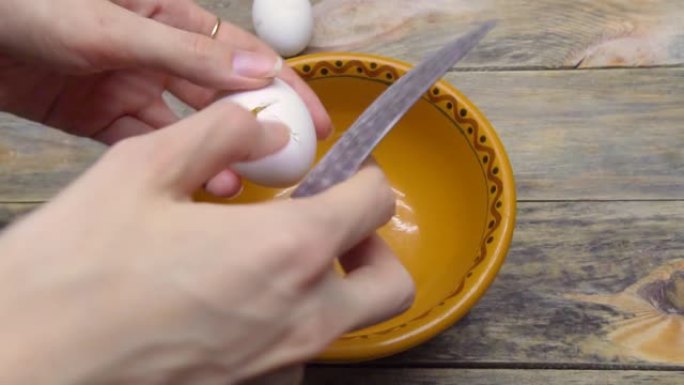 女人在木制背景上的盘子里打碎鸡蛋，以进一步烹饪
