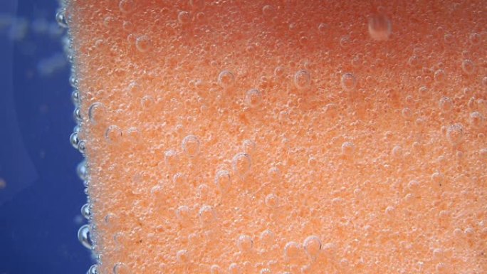 用于洗碗的橙色海绵，或带有气泡的身体海绵，在水下，选择性聚焦。卫生，宏观