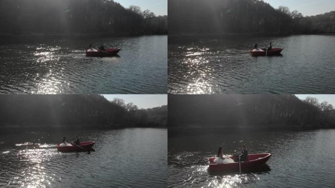 新娘在红船上游泳的空中镜头。明亮的太阳反射在湖中，形成反射和闪烁的眩光。