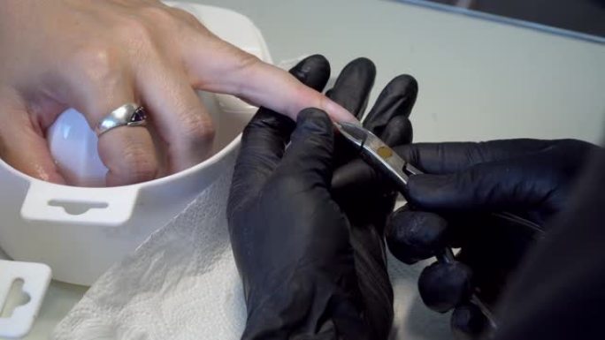 美容师在美甲沙龙用金属器械切割角质层。与角质层钳一起工作的美甲师。指甲大师用指甲刀去除角质层。美容院