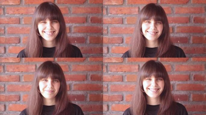一个穿着黑色t恤的刘海美丽黑发女人的肖像，她在砖墙背景上快乐微笑