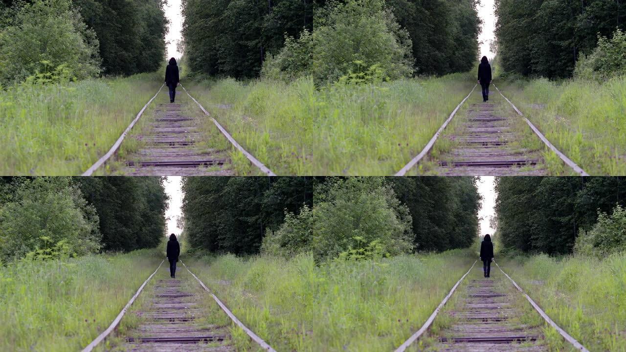 一个孤独的黑衣人正走在树林里的铁轨上，向后看。他感到放松、思考和无聊