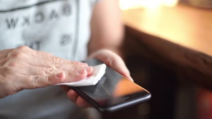 女性使用酒精喷雾和擦拭智能手机表面清洁和保护新型冠状病毒肺炎