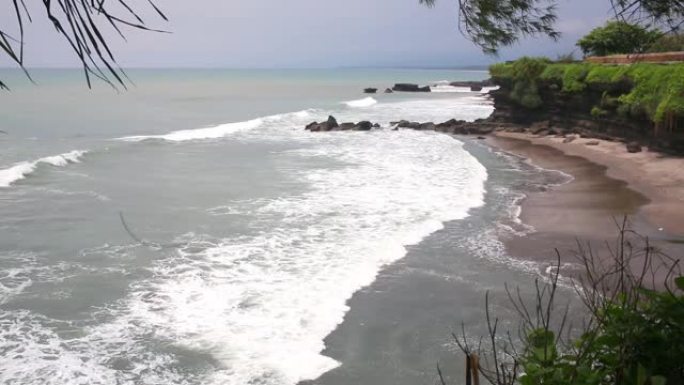 傍晚海面的空中静态视图，平静的海浪在多岩石的海岸滚动。海洋上方惊人的高崖和顶部的乌鲁瓦图神庙。印度尼