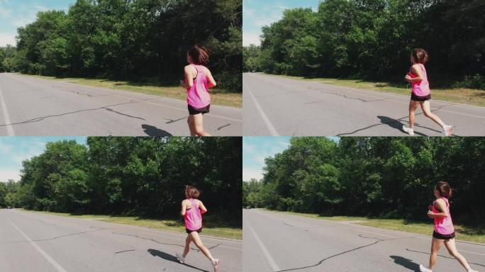 年轻迷人的女跑步者。穿着粉色衬衫的美丽上进心女孩正在城市公园跑步。带耳机的运动女性在公园训练