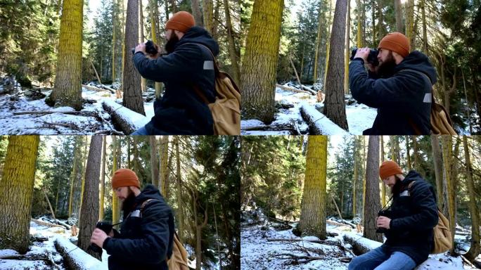 一位大胡子的男性旅行者摄影师在冬季森林中拿着相机拍摄大自然的照片。博客作者和摄影艺术家的旅行概念