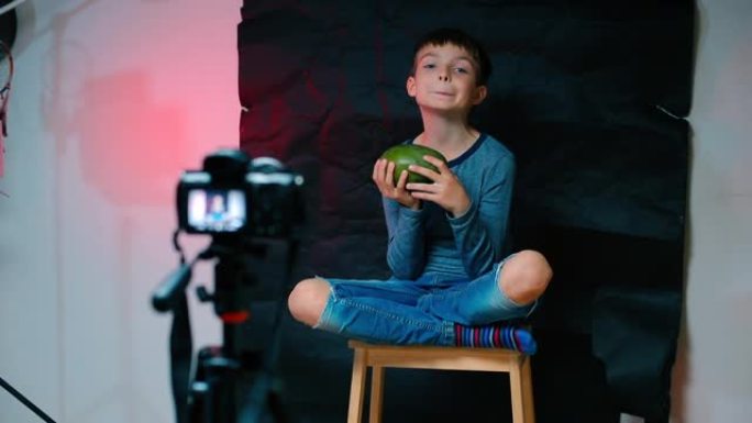 一个男孩坐在摄像机前，拿着芒果