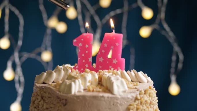 蓝色背景上有14号粉色蜡烛的生日蛋糕。蜡烛着火了。慢动作和特写视图