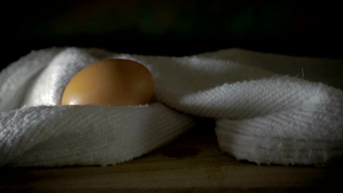 一只手用棉布从木制砧板上捡起棕色鸡蛋