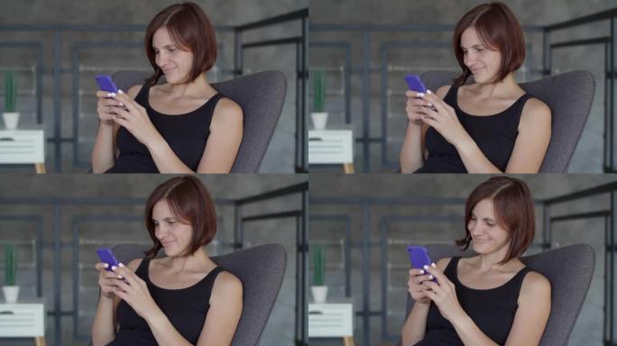 30多岁的年轻女性很高兴坐在舒适的沙发上用智能手机聊天。穿着黑色连衣裙的迷人女性在手机上自拍