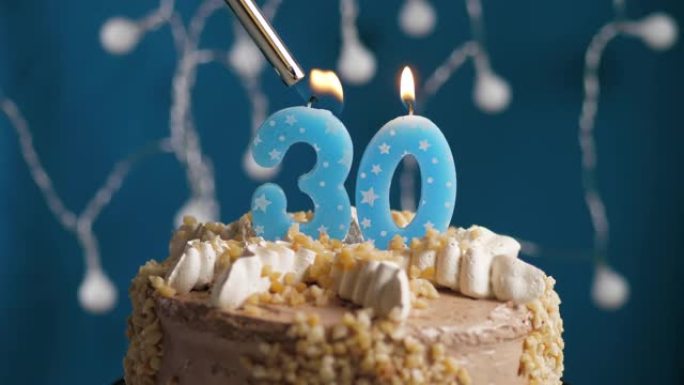 蓝色背景上有30号蜡烛的生日蛋糕。蜡烛着火了。慢动作和特写视图