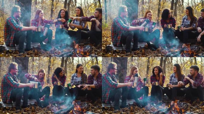 在秋天的森林中，年轻的游客坐在火炉旁坐着保温杯
