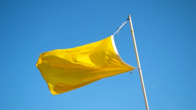黄旗在蓝天的沙滩上随风飘扬。慢动作。高清