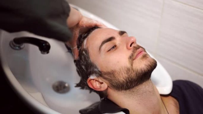 女人涂洗发水按摩头发顾客男人在美容院洗头发。快乐的高加索人享受理发店的服务