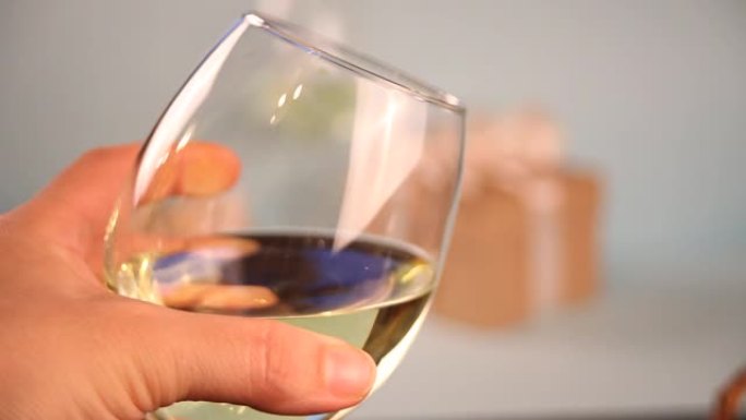 女人的手拿着一杯白葡萄酒。背景上的礼品盒。浪漫晚餐概念