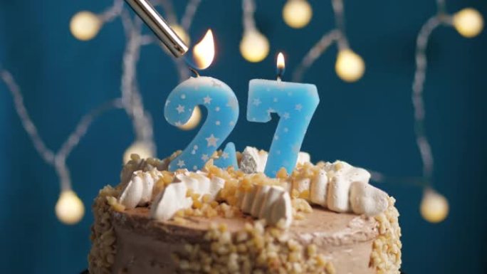 蓝色背景上有27个数字蜡烛的生日蛋糕。蜡烛着火了。慢动作和特写视图