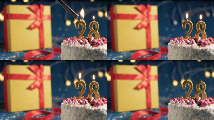 白色生日蛋糕编号28点灯燃烧的金色蜡烛，带灯的蓝色背景和用红丝带绑起来的礼物黄色盒子。特写
