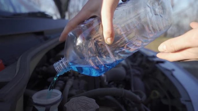 女人用整瓶防冻液用刮水器液手工填充汽车储液罐