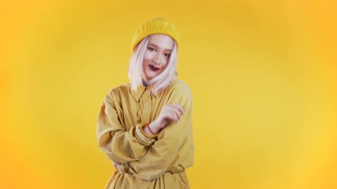 白发漂亮的年轻女孩站在黄色的工作室背景上，微笑着调情。带穿孔的不寻常女人的可爱肖像