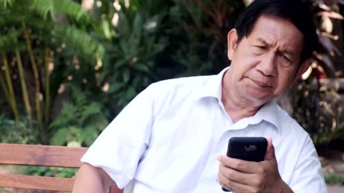 老人坐在公园长椅上使用手机。亚洲男人，浏览和切片手机。